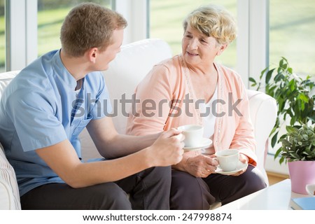 Young handsome male nurse and senior woman during tea time