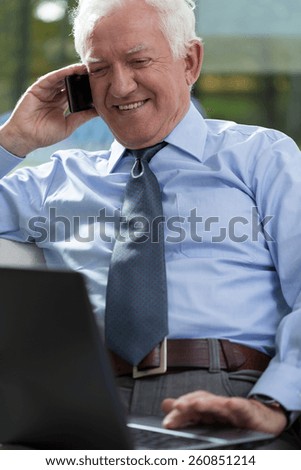 Elderly businessman working on laptop and talking phone