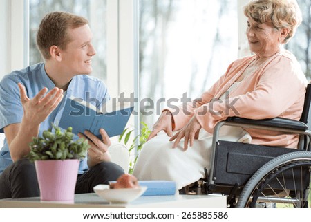 Male care assistant reading senior woman book