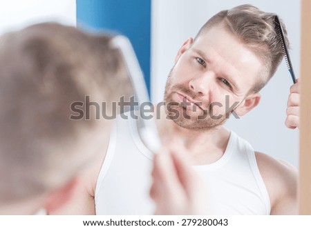 Reflection in the mirror of handsome man styling hair