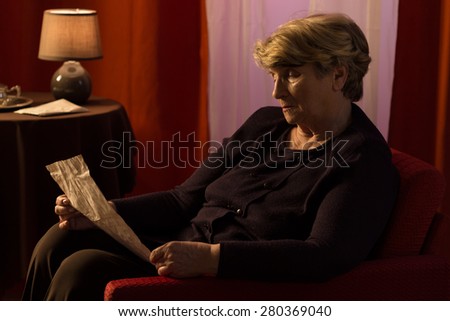 Elderly melancholic woman reading letter from old friend