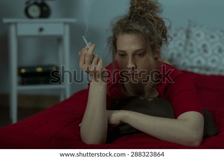 Young depressed woman is smoking in her  bed