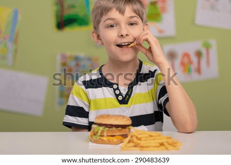Happy boy eating unhealthy french fries for lunch