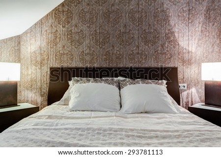 Comfortable bed and brown wallpaper in elegant bedroom