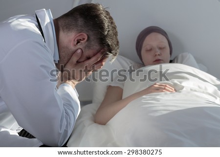 Broken down physician crying by sick young patient\'s bed