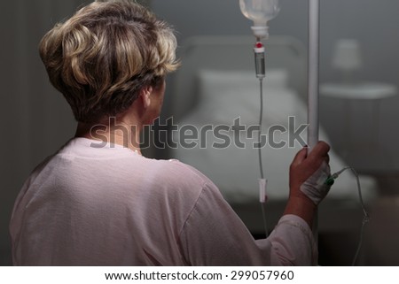 Sick older woman with drip walking in hospital