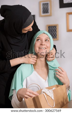 Pretty blond caucasian girl trying her muslim friend hijab