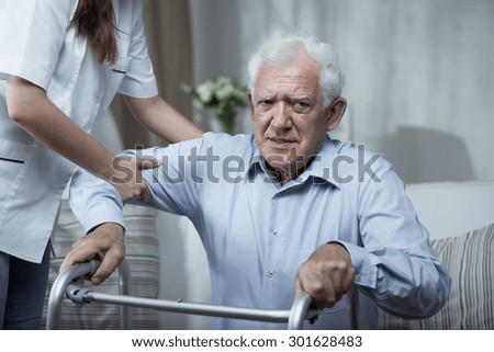 Physiotherapist helping disabled senior man with standing