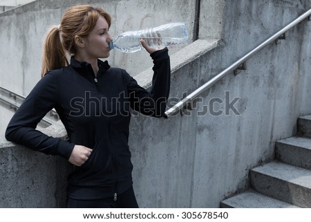 Female jogger standing by the stairs drinking water