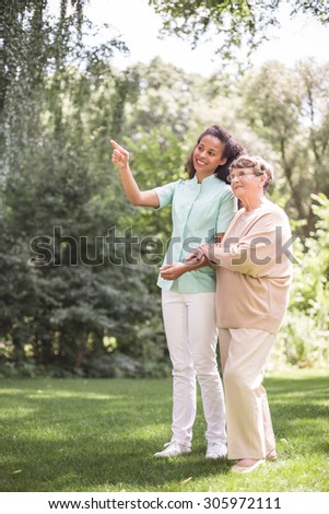 Elder woman and nurse strolling in the park