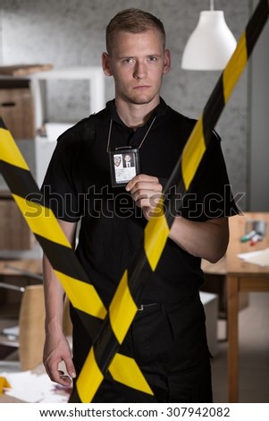 Policeman standing behind warning tape and showing police badge