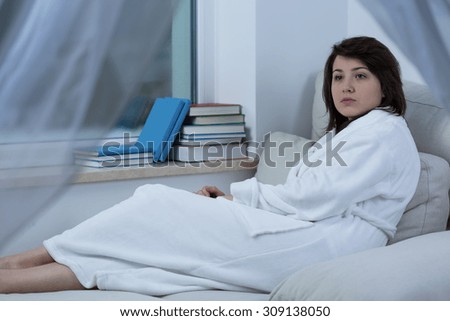 Young pretty sad woman in dressing-gown lying on a couch