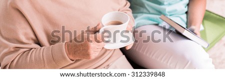 Panorma of elderly woman drinking coffee and her private caregiver