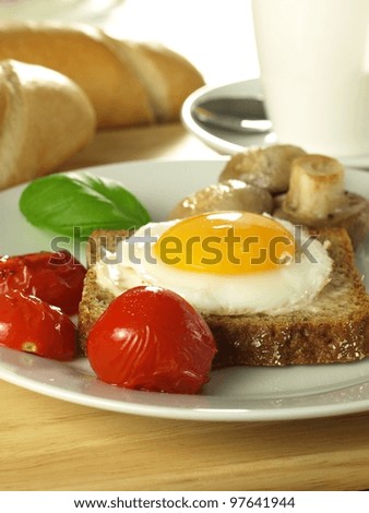 Sunny side up egg on a slice of bread with tomatoes and mushrooms with a French loaf.