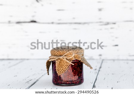 Raspberry jam in a jar on the wooden table