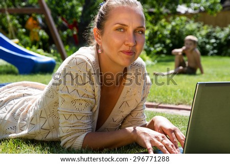young beautiful mother works as a freelancer at home, on the green lawn in your garden, through the Internet, While her children play nearby.