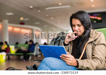 Hispanic young woman reading on a tablet while waiting to travel in airport terminal gate
