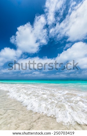 Turquoise waters and gentle waves of a white sand Caribbean beach with deep blue sky.