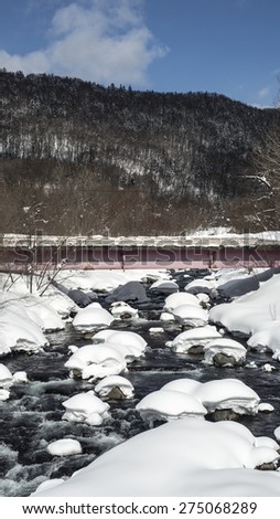 A river crosses under a bridge with snowy rocks in Mount Ashaidake Hokkaido, Japan