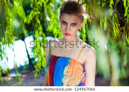 Young model posing in a bright dress on a beach near the deciduous tree