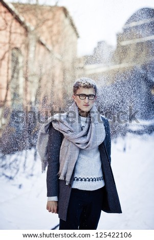 Stylish man in a coat and glasses throws the snow in front of you