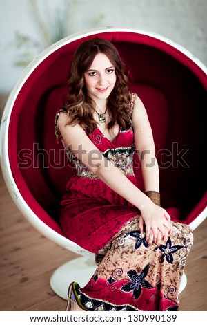 Smiling glamorous girl in a light dress sitting in a chair ball