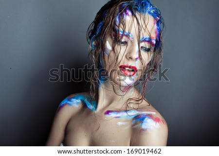 Creative art makeup of a young girl with blue eyes. Strokes of paint on his face and hair. Wet hair on her face