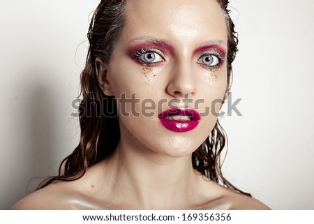 Cute young girl with creative make-up art. Glitter on her face, monochrome eyelashes, wet hair and fuchsia lips