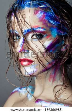 Creative art makeup of a young girl with blue eyes. Strokes of paint on her face and hair. Wet hair on her face