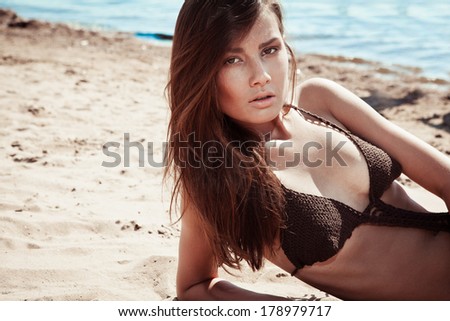 Beautiful young brunette woman on a sunny beach in a brown knit bikini