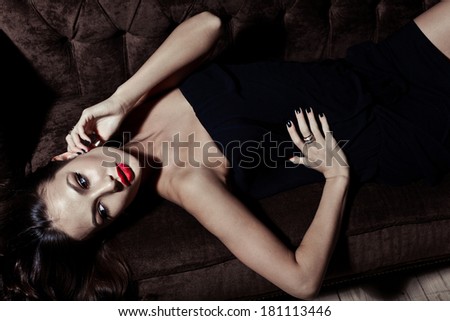 sensual elegant young woman in black dress on sofa indoor shot