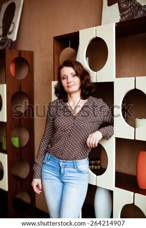 Middle-aged woman in jeans and a blouse standing near shelves