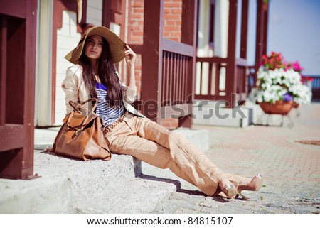 Photo of a young beautiful woman brunette fashion fabrics in today's casual elegant hat with a bag