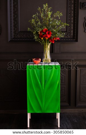 Bouquet of red calla lilies in a glass vase with a pomegranate and eucalyptus stands on the bedside table on a black background