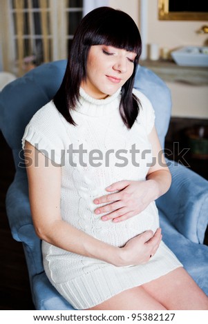 Pregnant woman in a sweater and socks sitting in a armchair