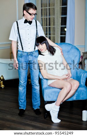 Pregnant woman in a sweater and socks with her husband sitting in a armchair