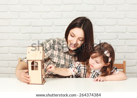 Young mother and daughter with little wooden house. Family, investment and payment concept. Girl trying to open house with wooden key.