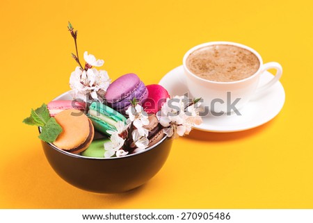 Colorful macaroon in bowl with flowers and coffee on bright background