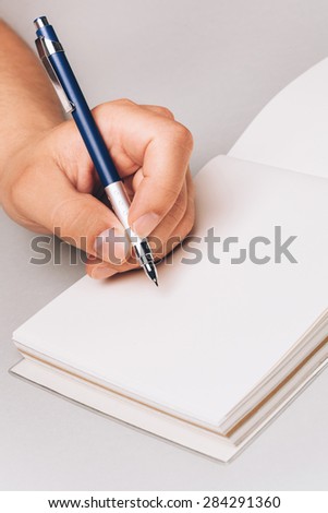 Man, holding pen in his hand and writing something in his note book. Place for text, closeup.