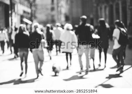 Blurred crowd of walking people in the city with buildings in the background, black and white