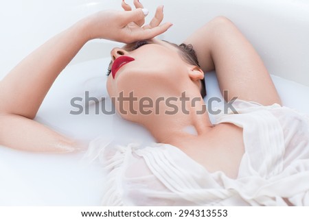 Beautiful young girl in a white blouse lying in the bathroom with white water, milk , passionately bent and touching his forehead with his hand
