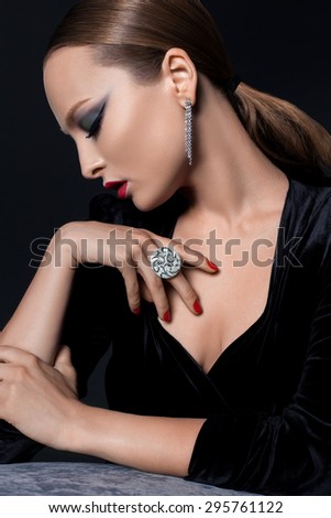 Portrait in profile of a young woman , blonde , Europeans , dressed in a black dress and a shot on black background, decorated with earrings and ring