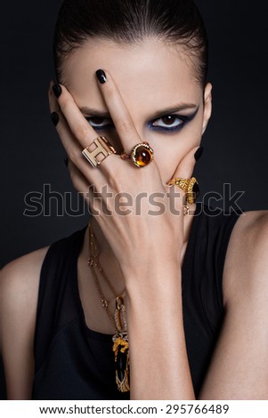Portrait of a young , beautiful girl Europeans , with bright makeup and brushed the hair covering the face with his hand , a lot of a lot of jewelry on the fingers ,Lux fashion