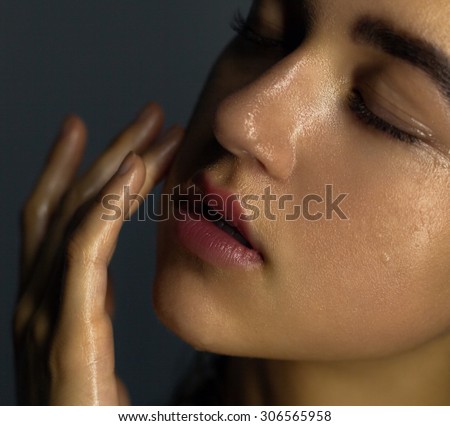 Beauty portrait of a young girl with clean skin on a dark background , brush gently touch his cheek . Clean skin is covered with drops of moisture.