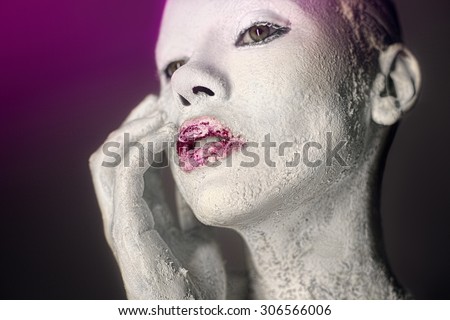 Beauty portrait of a young girl on a dark purple gradient background, fingers gently touch her ??cheek. The skin is covered with a white textured paint , bright magenta lips in a blaze