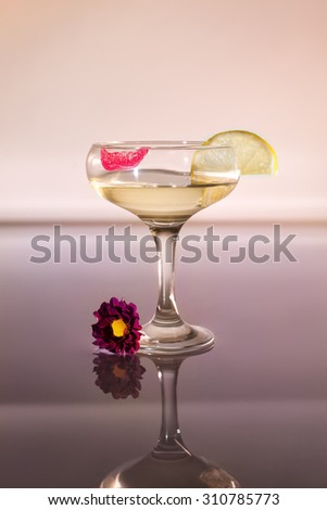 Vertical shot wide glasses with champagne , where the red imprint of lipstick and a slice of lemon , baud flower lies at the foot of the glass, the reflection on the table.