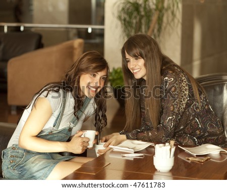 Two beautiful young women with great teeth enjoying their lunch break, drinking coffee, sharing a secret.