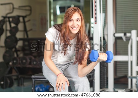 Happy young women doing bicep curl in the gym smiling to the camera
