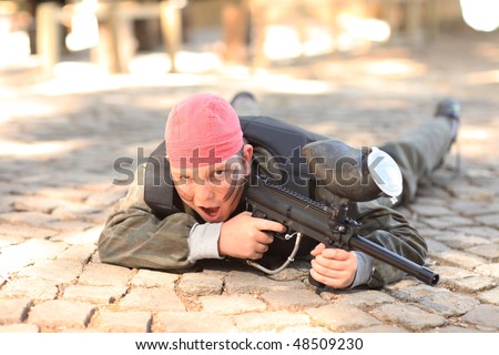 Boy with uniform, red bandana and paintball gun in hand posing for the camera