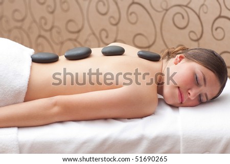 Beautiful young woman enjoying a hot mineral stone treatment in spa, shallow depth of field, focus on stones